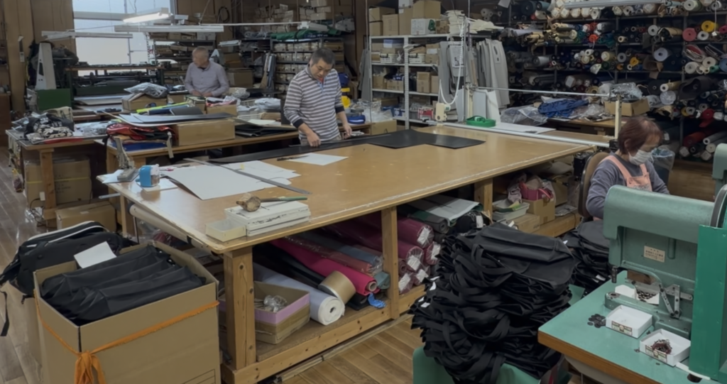 縫製工場の作業台で型紙や素材を準備しながらバッグ製作を進める作業風景
