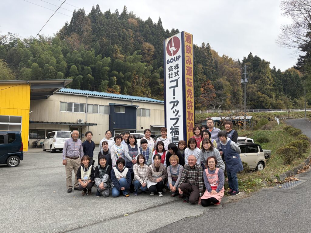 福島の自然に囲まれた縫製工場前で撮影されたスタッフ集合写真